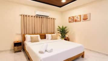 A hotel room with a large bed, an air conditioning unit, a nightstand, and a potted plant.
