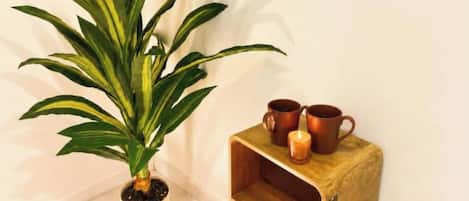 A potted plant, two copper mugs, and a candle on a wooden nightstand.