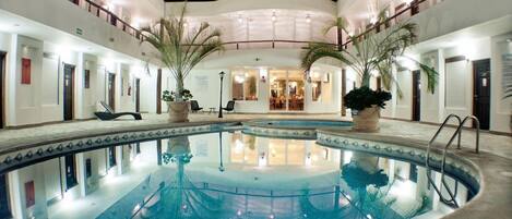 A hotel pool area with a central pool, palm trees, and a dining area in the background.