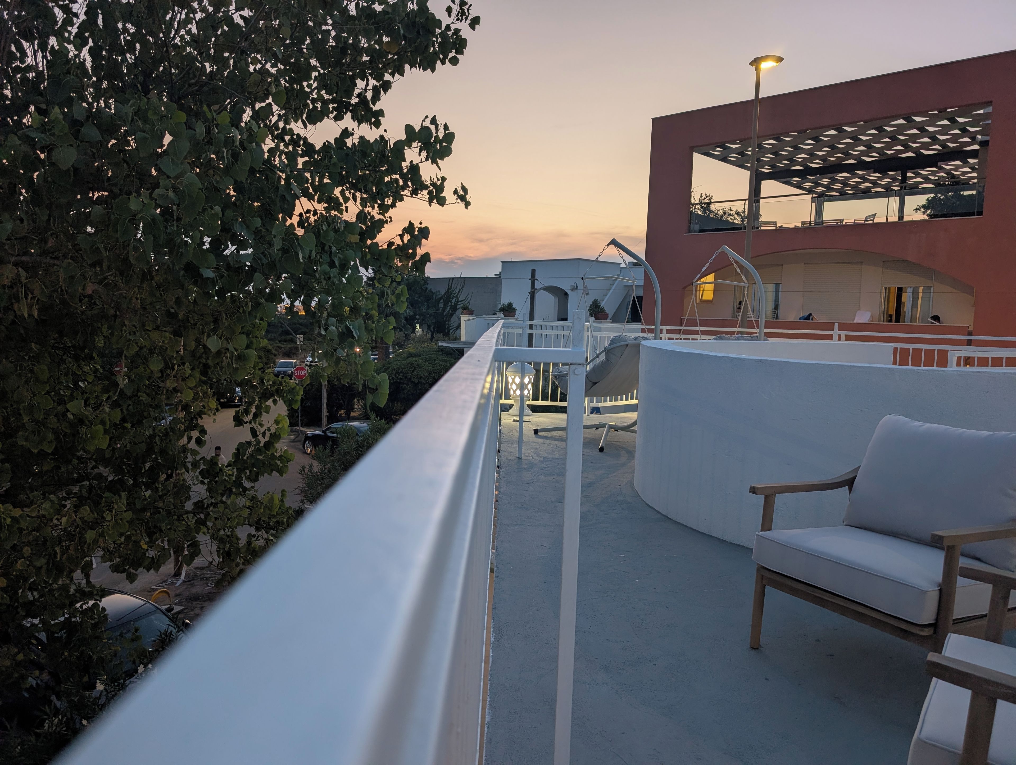 A balcony with a white railing, a swing, and a seating area with a cushion.