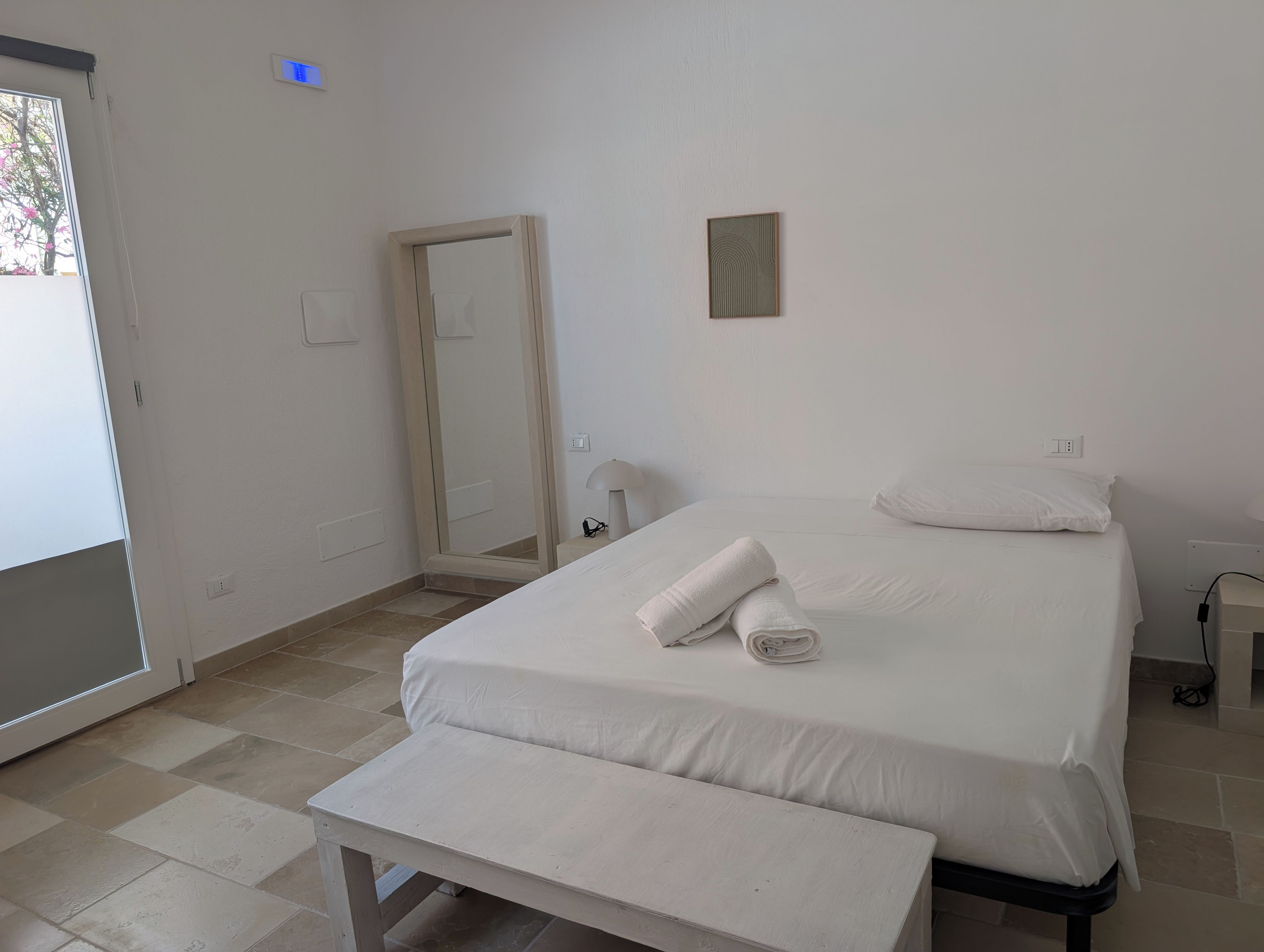 A hotel room with a bed, a bench, a mirror, and a door.