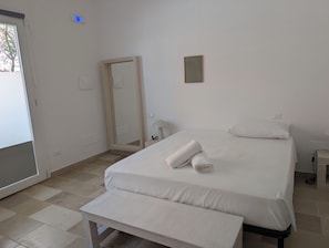 A hotel room with a bed, a bench, a mirror, and a door.
