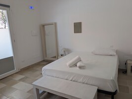 A hotel room with a bed, a bench, a mirror, and a door.
