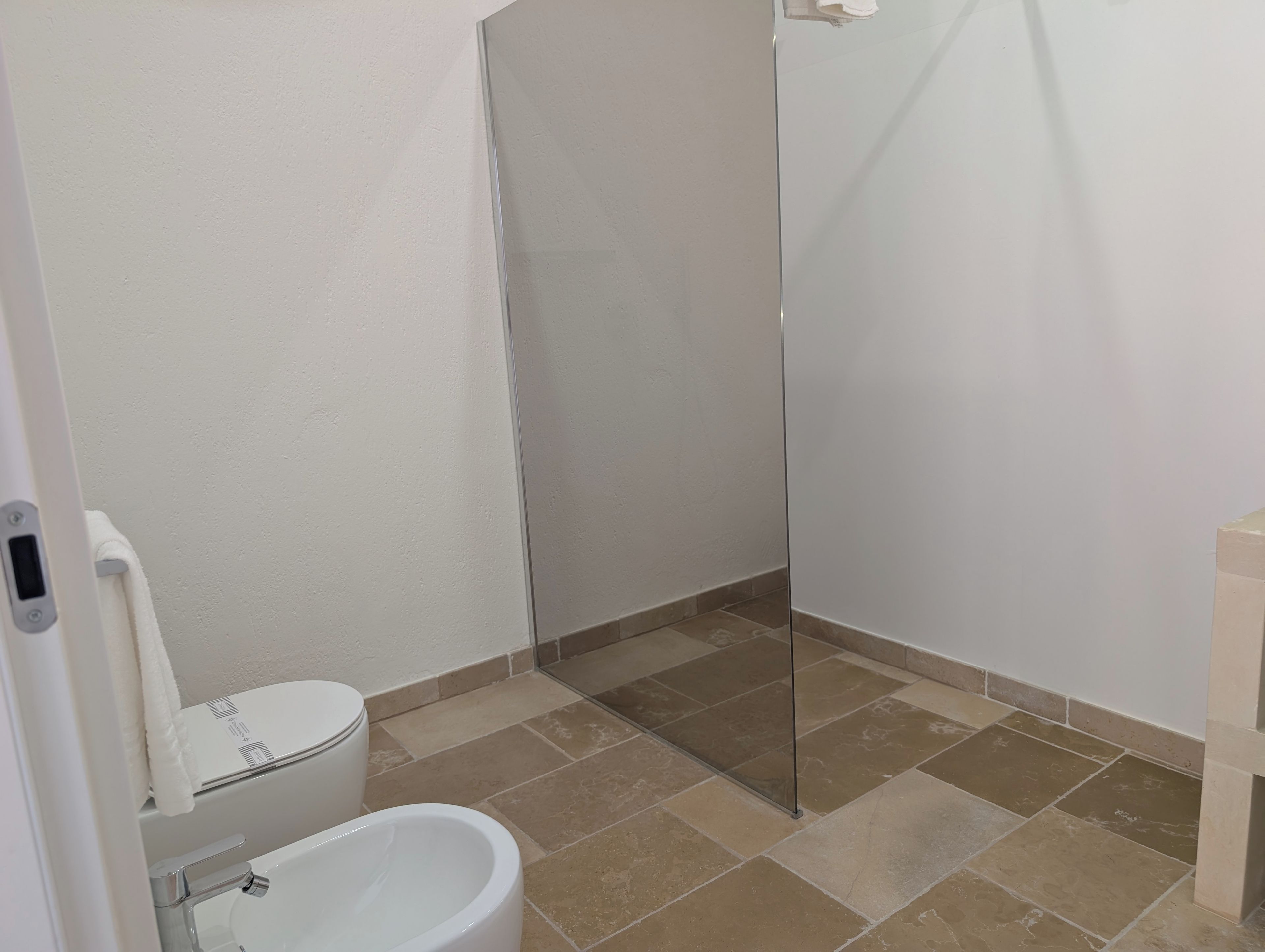 Un baño con inodoro, bidé y cabina de ducha con mampara de vidrio.