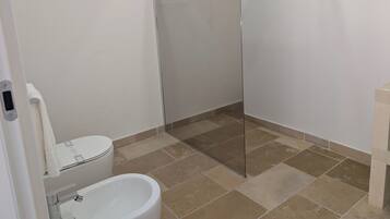 Un baño con inodoro, bidé y cabina de ducha con mampara de vidrio.