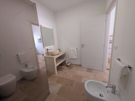Un baño moderno con inodoro, bidé, lavamanos y espejo.