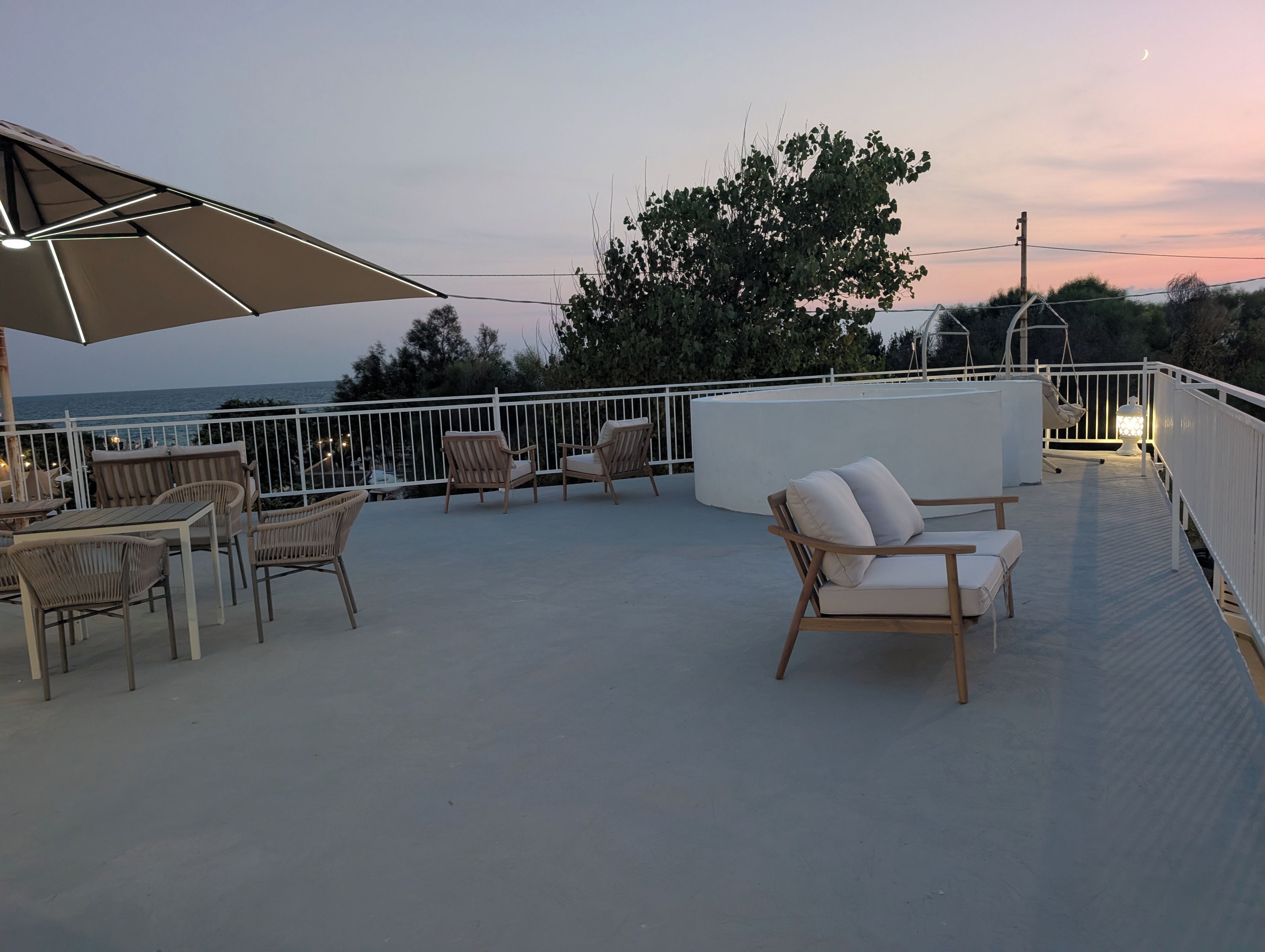 A rooftop terrace with outdoor seating, a view of the sea, and a sunset in the background.