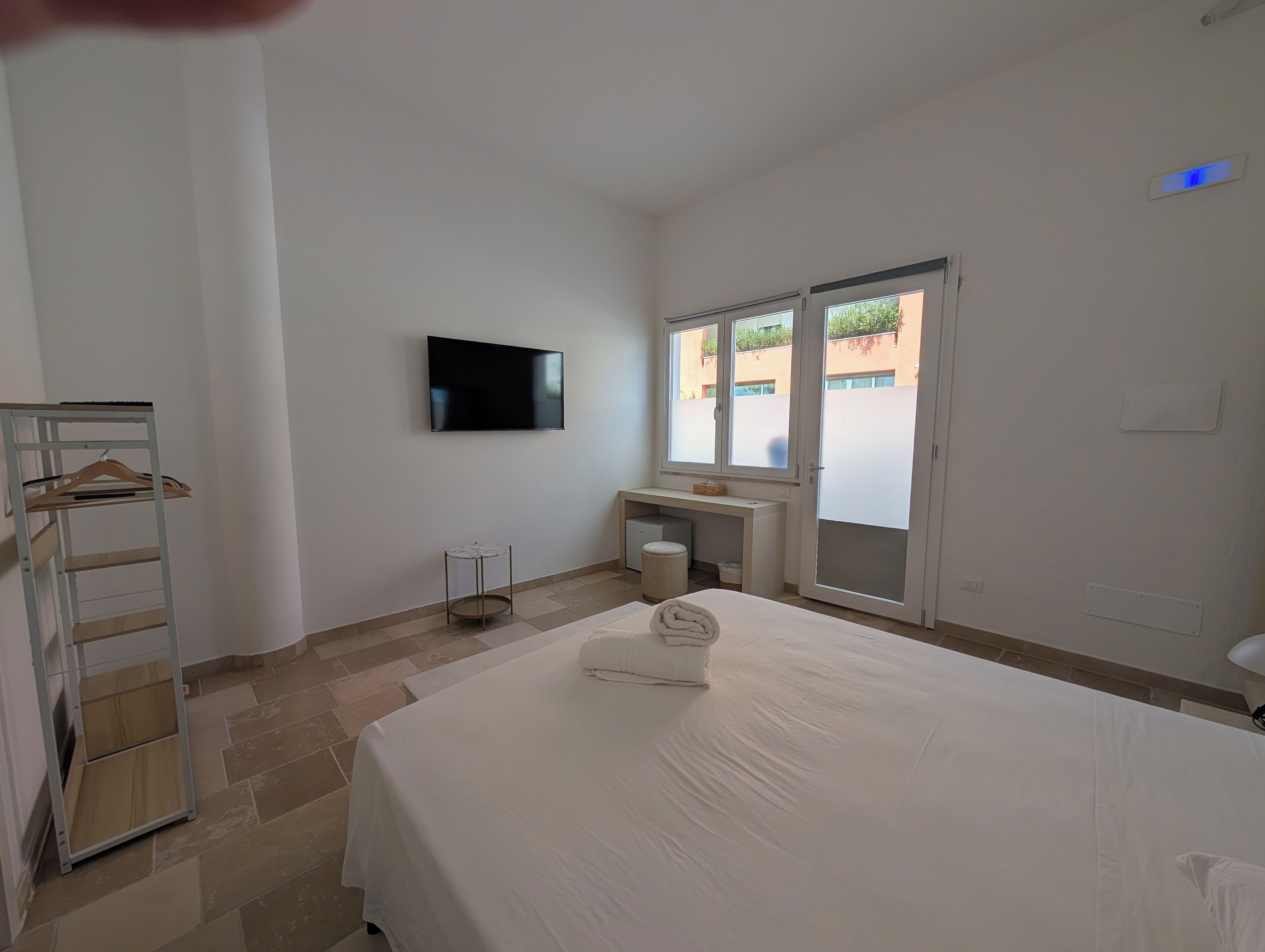 A hotel room with a bed, a TV mounted on the wall, a desk, and a window.