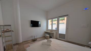 A hotel room with a bed, a TV mounted on the wall, a desk, and a window.