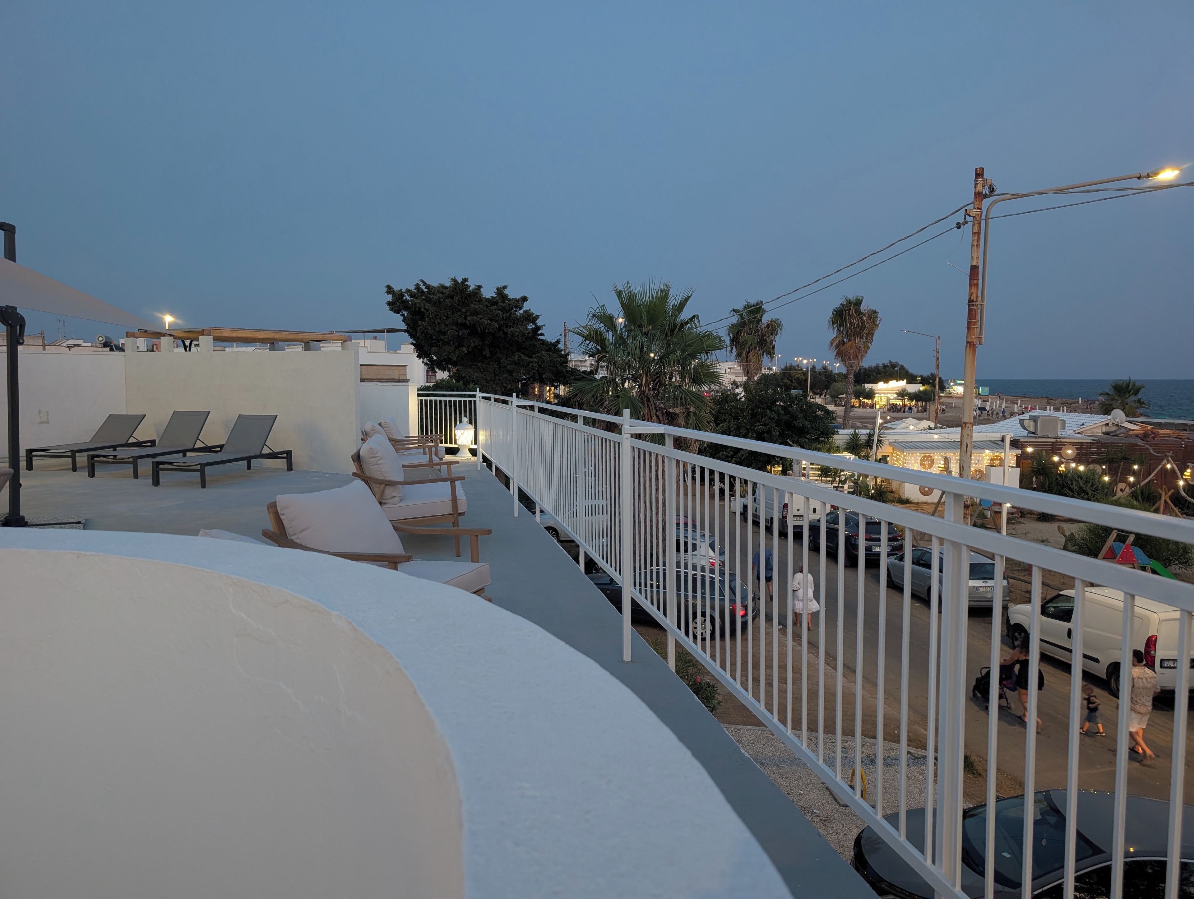 Terraza en la azotea con sillones de descanso y barandilla, con vista a una calle con coches aparcados y edificios.