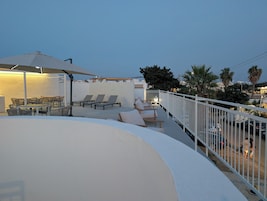 Una terraza en la azotea con mobiliario exterior, barandilla blanca y vistas a la ciudad.