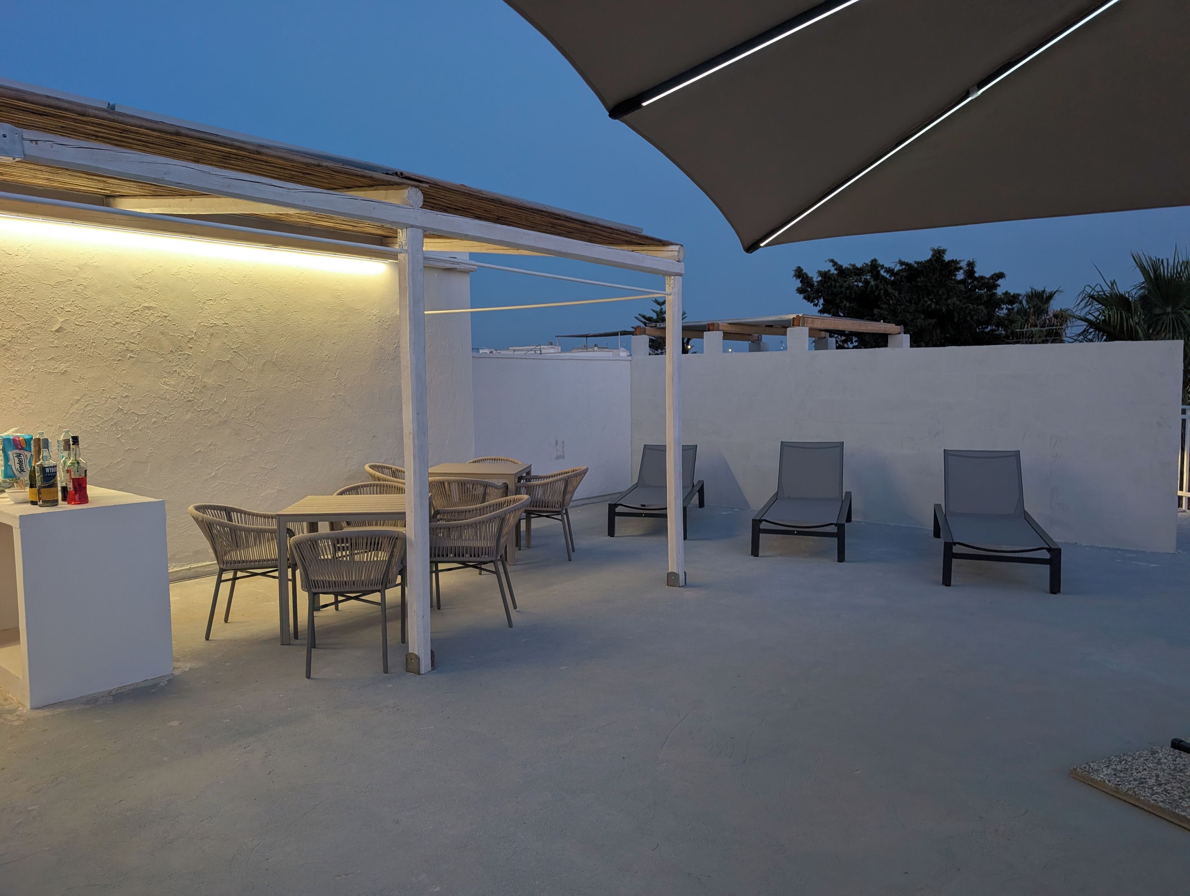 An outdoor patio with a white wall, a table with chairs, and a bar area with bottles.