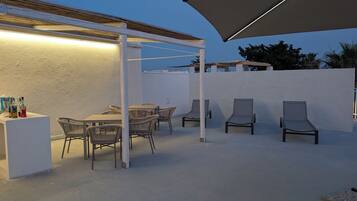 An outdoor patio with a white wall, a table with chairs, and a bar area with bottles.