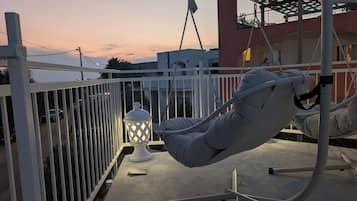 Un balcón con una silla colgante, un farol blanco y una señal de stop al fondo.