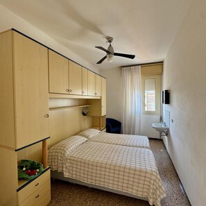 A bedroom with a bed, a wardrobe, a ceiling fan, a window with curtains, and a sink. - Arborea (Jesolo)