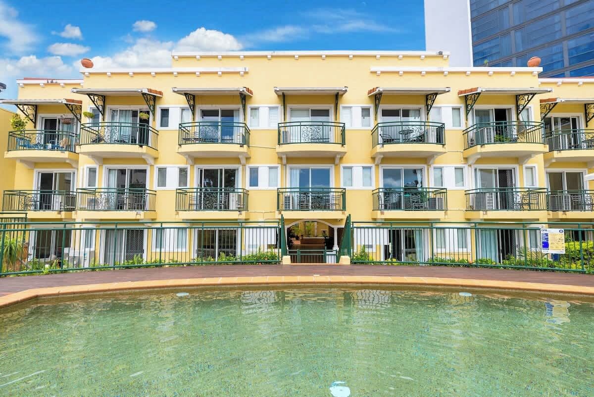 Un hotel de varios pisos con balcones, piscina y cielo despejado.