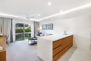 A modern kitchen with a central island, a dining area with a round table, and a sliding glass door leading to a patio. - Cairns Central, your modern Oasis with pool (Cairns City)