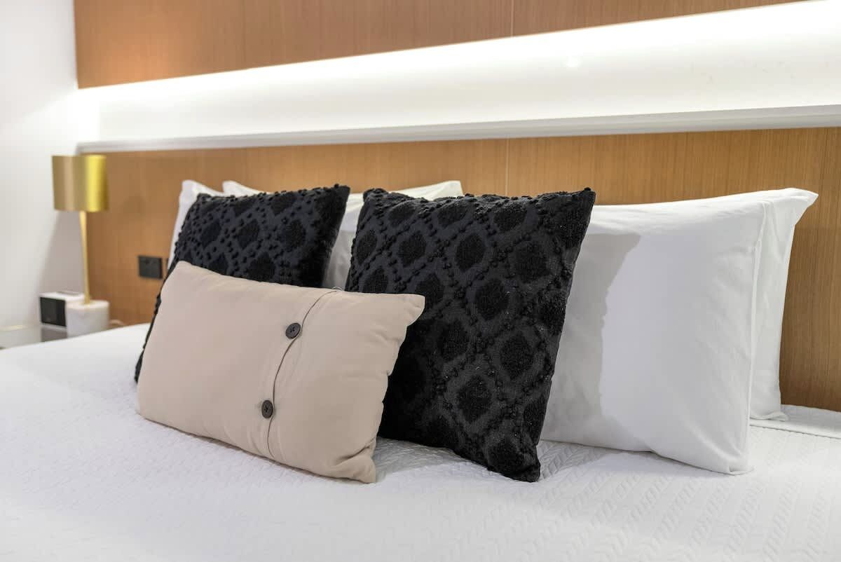 Una habitación de hotel con una cama, dos almohadas estampadas, una almohada lisa y una lámpara de noche.
