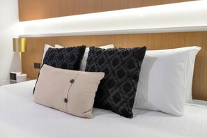 Une chambre d’hôtel avec un lit, deux coussins à motifs, un coussin uni et une lampe de chevet.