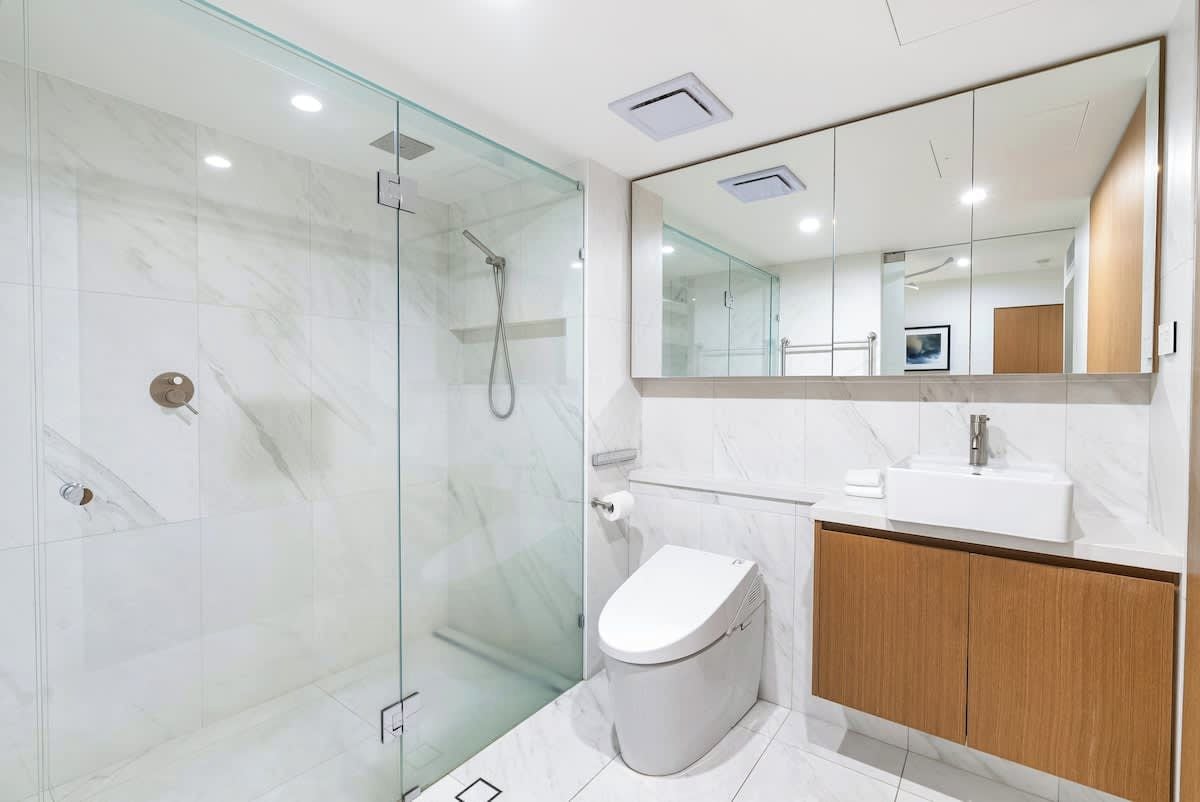 Un baño moderno con ducha de vidrio, inodoro, lavamanos y un espejo grande.