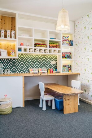 A children's play area with a wooden table, white chairs, and shelves filled with toys and games. - Tulum Beach Resort & Spa Dakhla (Dakhla)