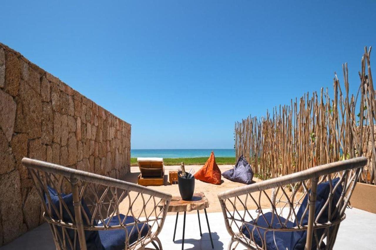 A beachside seating area with wicker chairs and a table, overlooking the ocean.
