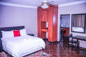 A hotel room with a bed, a desk, a chair, a wardrobe, and a ceiling fan.