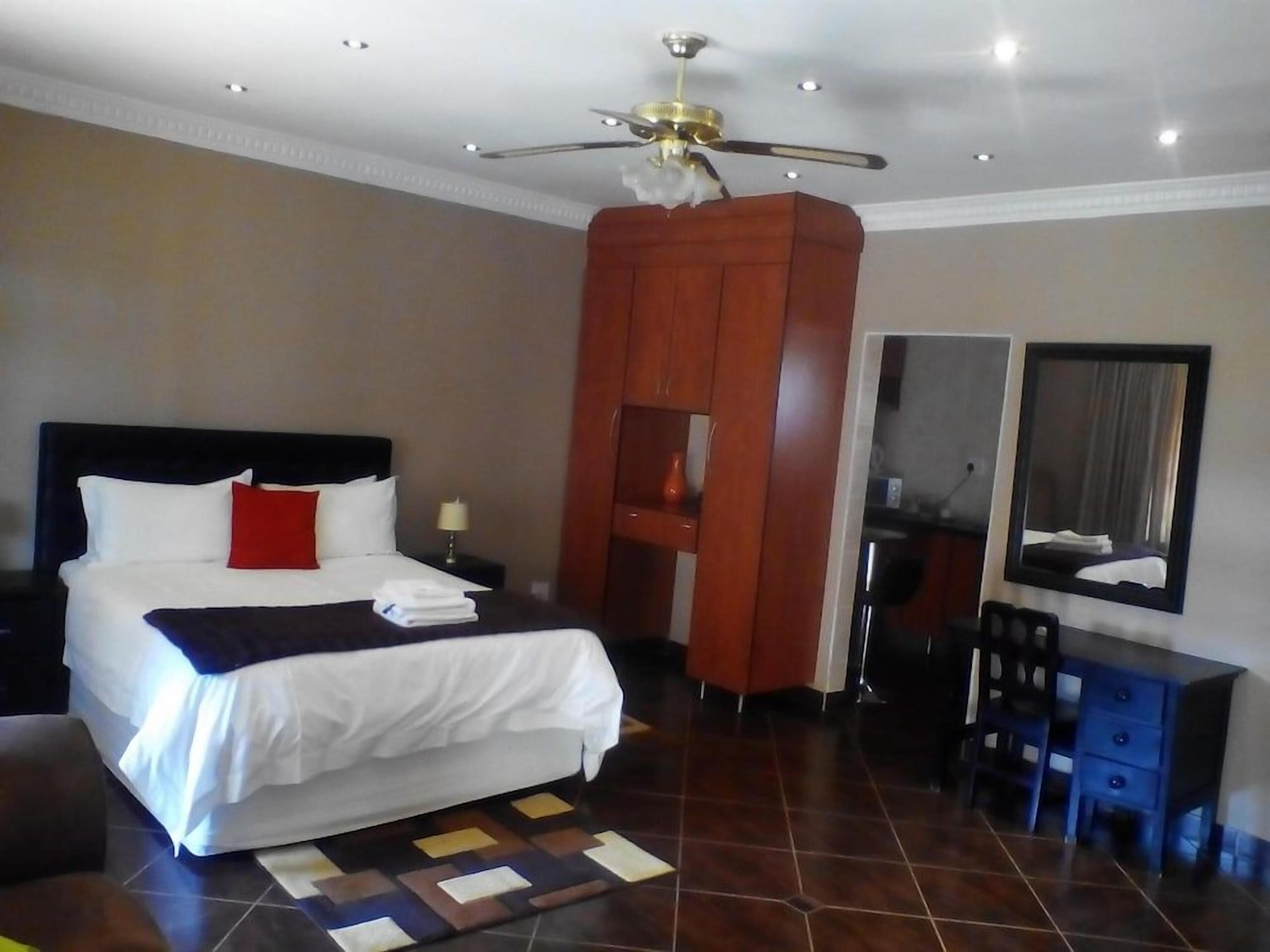 A hotel room with a bed, a desk, a chair, a ceiling fan, and a mirror.