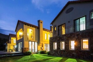 Un edificio residencial de varios pisos con fachada de piedra e iluminación exterior, y un balcón visible.