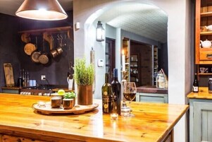 Zona de bar con mostrador de madera, botellas, vasos y un colgador para ollas.