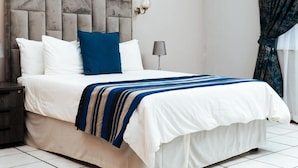A bed with a headboard, pillows, a bedside lamp, and a striped blanket. - Ngwenya City Hotel (Klerksdorp)