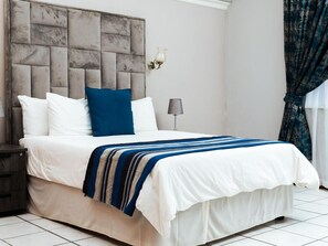 Un letto con testiera, cuscini, una lampada da comodino e una coperta a righe.