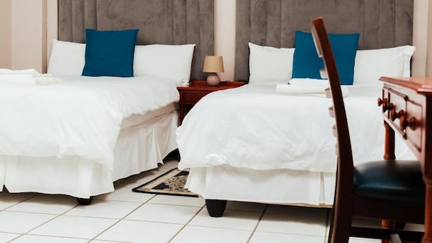 A hotel room with two beds, a nightstand, a chair, and a lamp. - Ngwenya City Hotel (Klerksdorp)