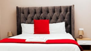 A bed with a tufted headboard, white bedding, and red accents. - Ngwenya City Hotel (Klerksdorp)