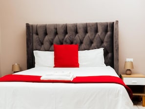 Un letto con testiera trapuntata, biancheria bianca e tocchi di rosso.
