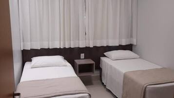 Quarto de hotel com duas camas, uma mesa pequena e uma janela com cortinas.