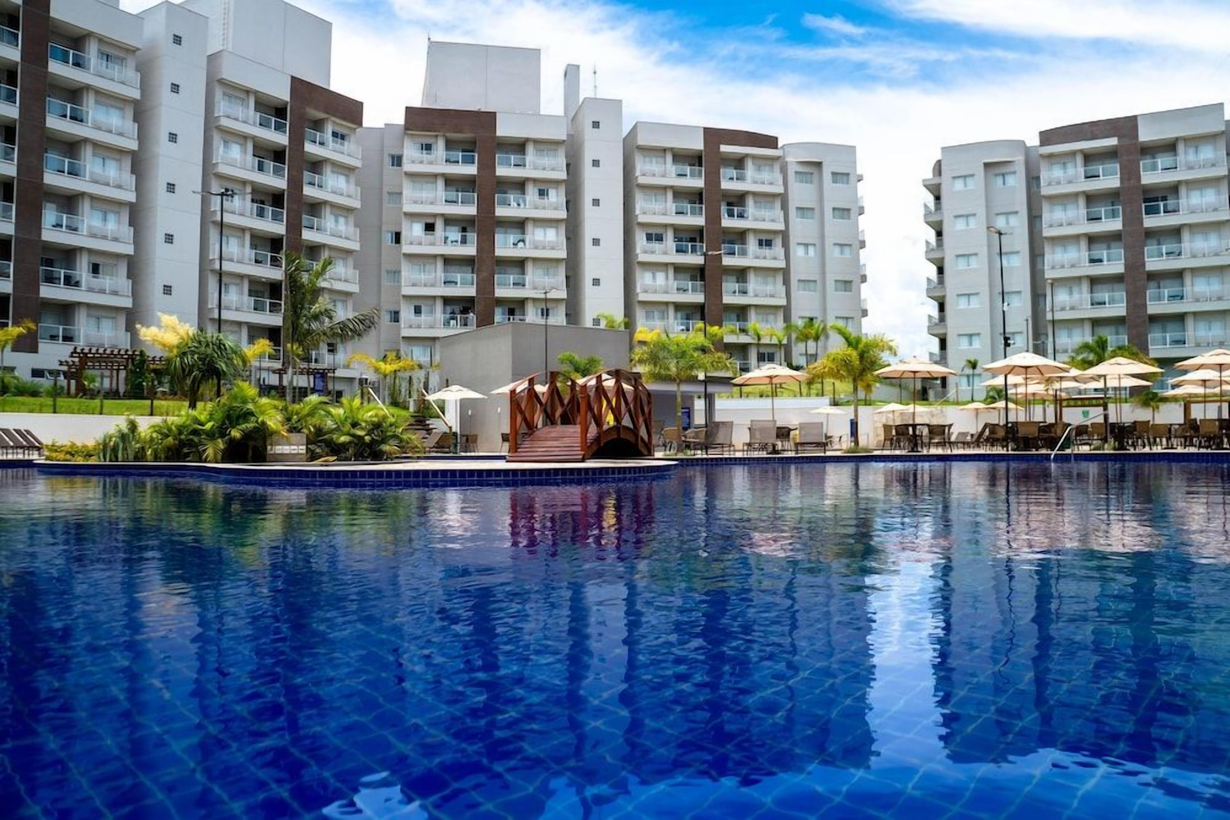 Piscina com superfície de água azul translúcida, cercada por área de lazer com guarda-sóis e espreguiçadeiras.