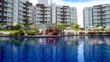 Piscina com superfície de água azul translúcida, cercada por área de lazer com guarda-sóis e espreguiçadeiras.