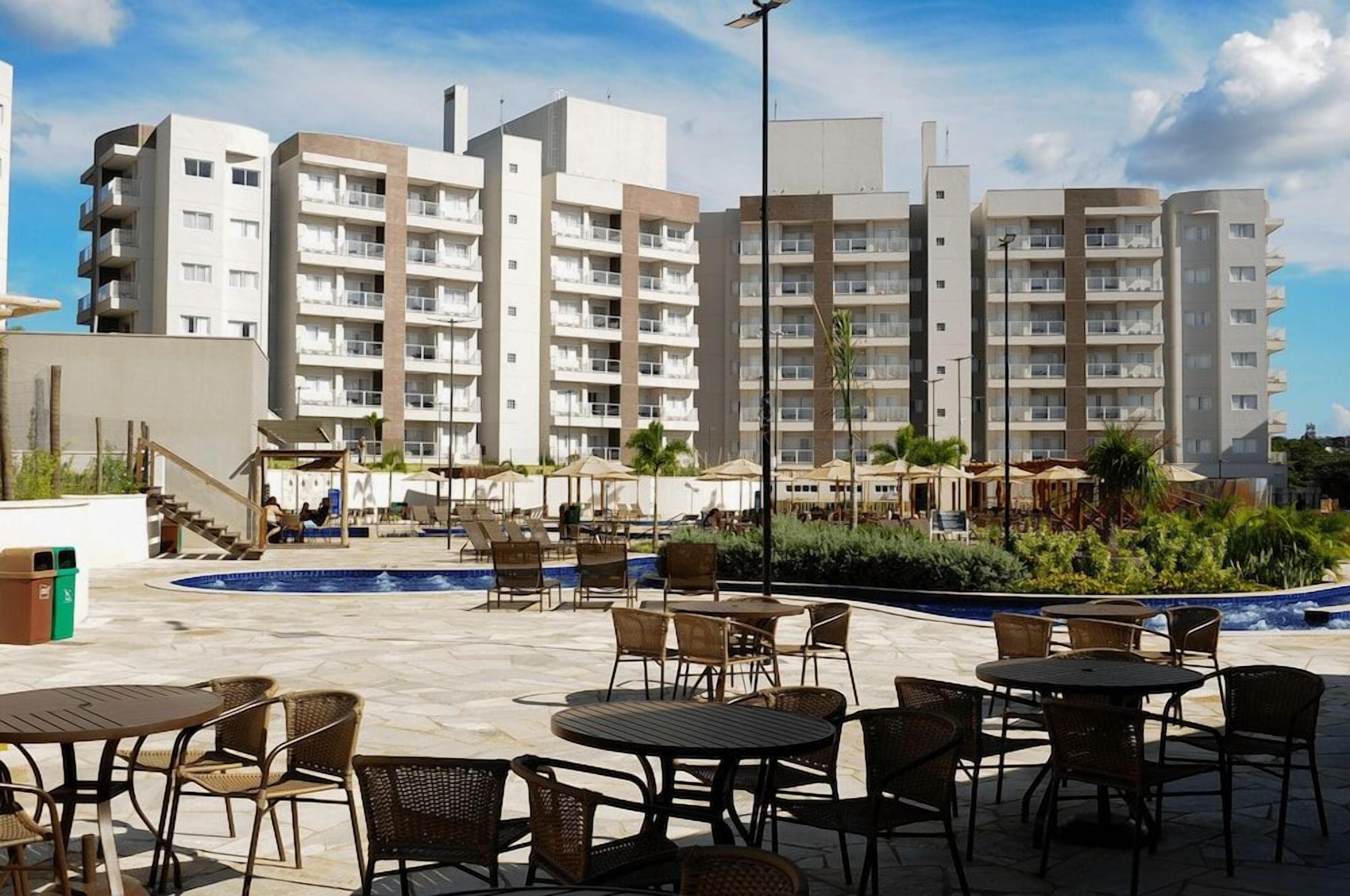 Pátio de hotel com área de estar externa, piscina e edifícios altos ao fundo.