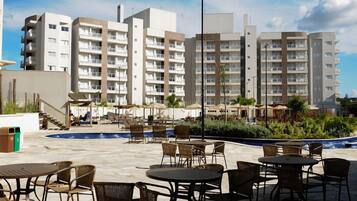 Pátio de hotel com área de estar externa, piscina e edifícios altos ao fundo.