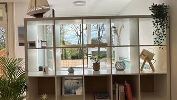 A modern living room with a large bookshelf, a hanging lamp, and a view of the outdoors.