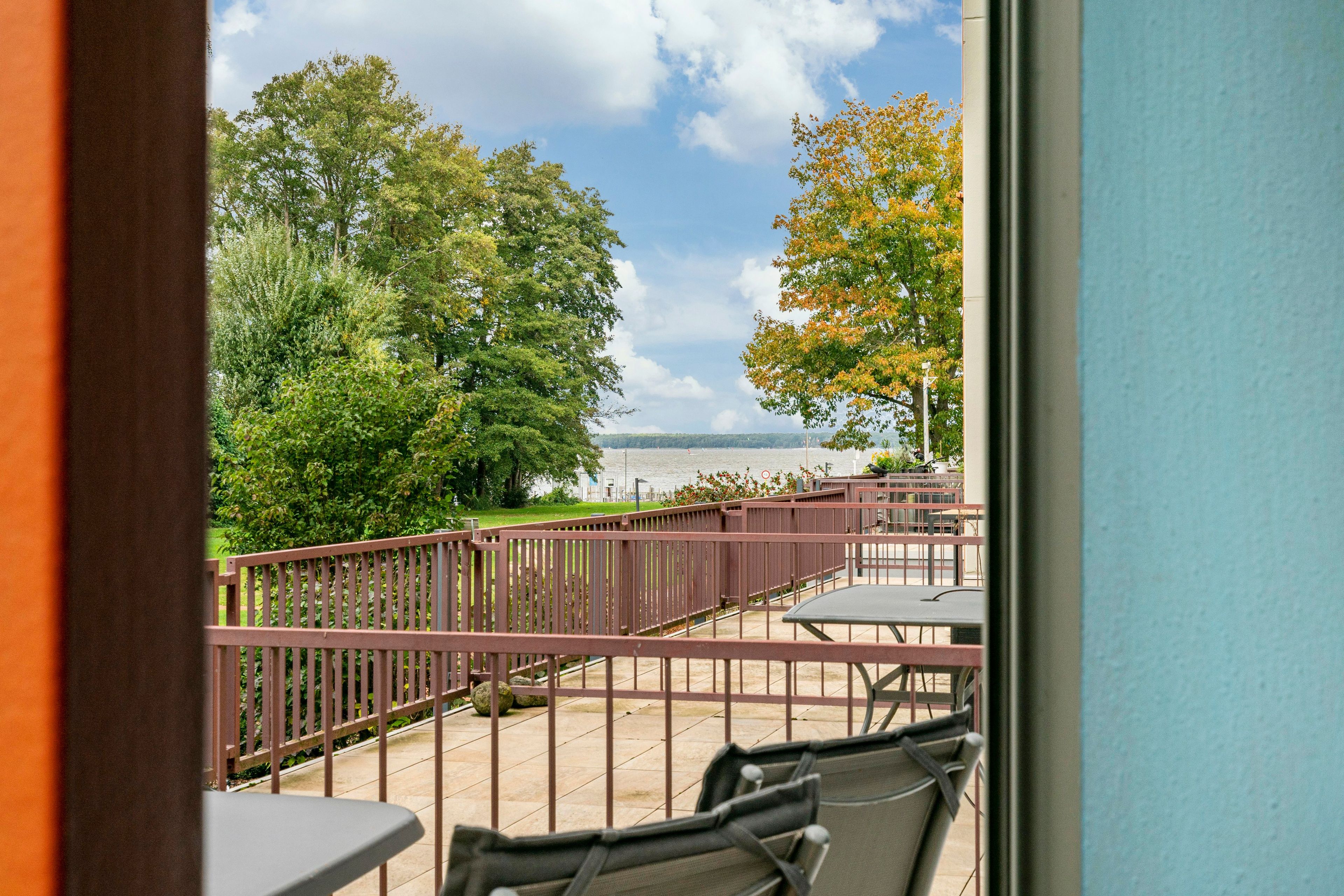 Ein Balkon mit Blick auf ein Gewässer, umgeben von Bäumen und einem Metallgeländer.