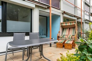 Un patio con mesa y sillas, una silla lounge de mimbre con cojines y vistas del exterior del edificio.