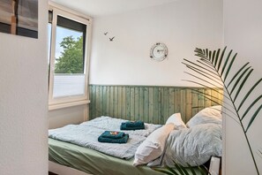 A bedroom with a bed, a window, a wooden headboard, a wall clock, and a plant. - Studio 'AhoiPause Steinhude' with Lake View, Terrace and Beach Chair (Wunstorf)