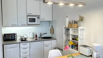 Eine kleine Küche mit weißen Schränken, einer Mikrowelle, einem Toaster und einer Kaffeemaschine.