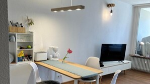 Et moderne opholdsrum med spiseplads, et fjernsyn og et køkken.