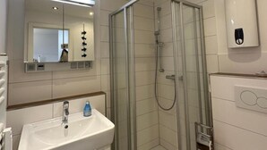 Et moderne badeværelse med en brusekabine i glas, en hvid vask og et toilet.