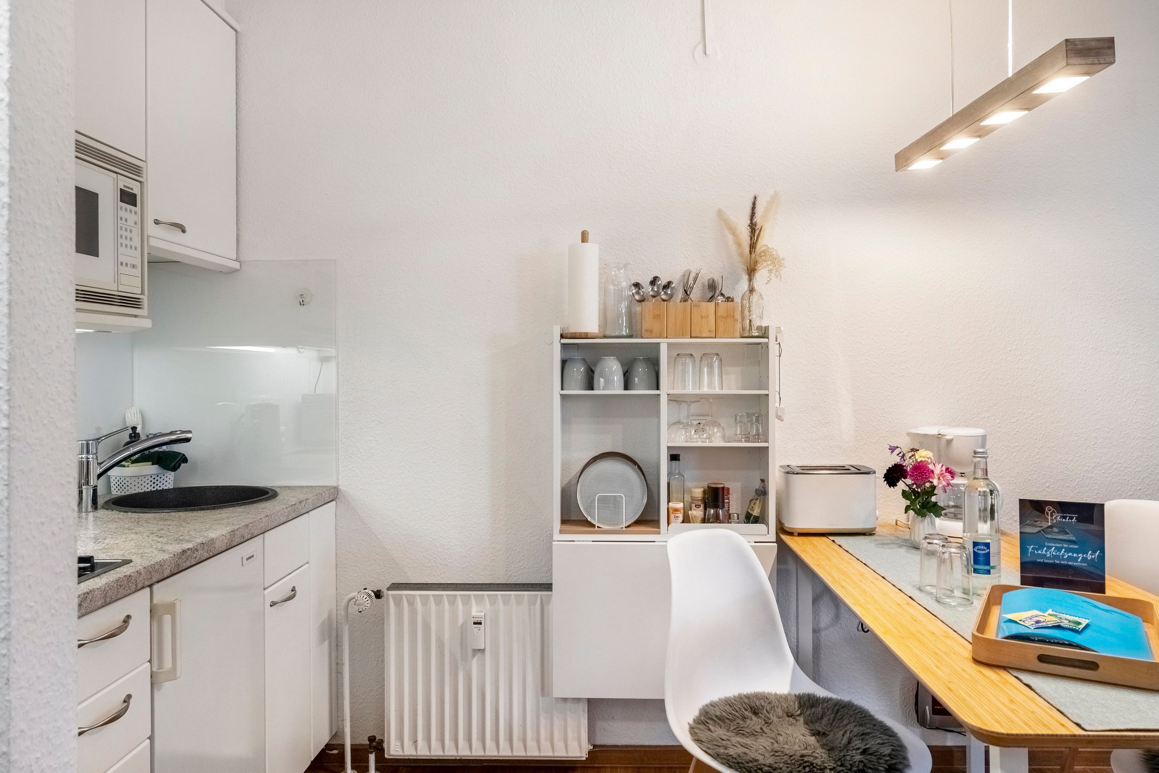 A compact kitchen with a built-in microwave, a sink, and a dining area with a chair and a small table.