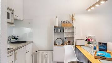 A compact kitchen with a built-in microwave, a sink, and a dining area with a chair and a small table.