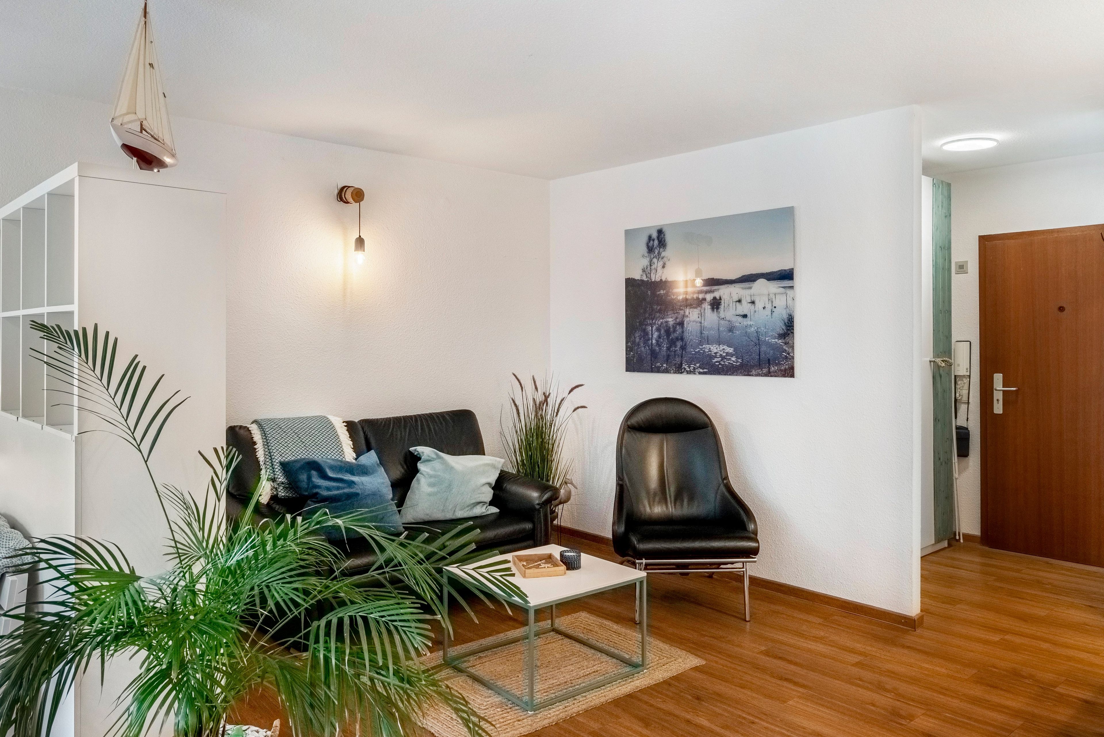A modern living room with a sofa, a coffee table, and a chair. There is a painting on the wall and a plant in the corner.